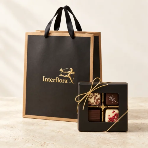 Svart presentpåse från Interflora med sidenhandtag och en svart chokladask med fyra praliner och guldsnöre.